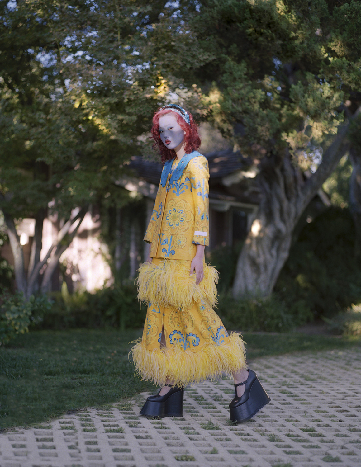 Full body shot of a model with blue facepaint and red lips outdoors in a garden setting